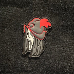 Puede incluir: Parche bordado en negro y rojo con una calavera que lleva un sombrero con una pluma roja. La calavera tiene la cara blanca y está rodeada de un diseño en blanco y negro.