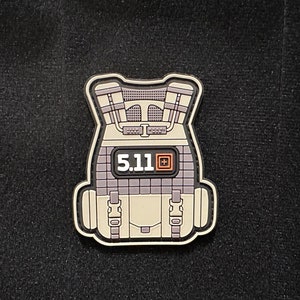 May include: A beige and gray tactical vest patch with the text "5.11" and a small orange square logo.