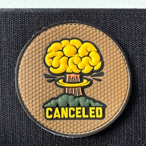Peut inclure: Un patch marron avec un motif hexagonal présente une explosion en forme de cerveau jaune avec le mot "CANCELED" en lettres jaunes.