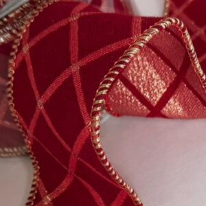 May include: A deep red velvet ribbon featuring a metallic gold grid pattern. The edges of the ribbon are finished with a twisted gold cord trim, creating a structured and decorative border along the length of the fabric material.