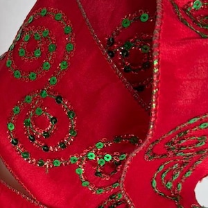 May include: A wide red ribbon featuring a repeating pattern of embroidered green sequin swirls. The ribbon has a wired edge with a subtle metallic gold trim, allowing it to be shaped into loops and folds while maintaining its structure.