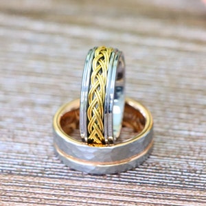 May include: Two wedding bands, one with a braided gold design and the other with a hammered finish.