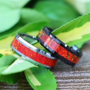 May include: Two black tungsten carbide rings with a red opal inlay. The rings are beveled and have a polished finish.