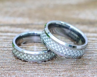 May include: Two silver wedding bands with a carbon fiber pattern. The bands are stacked on top of each other.