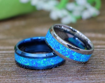 May include: Two blue and silver tungsten carbide rings with a blue opal inlay. The rings are on a wooden surface.