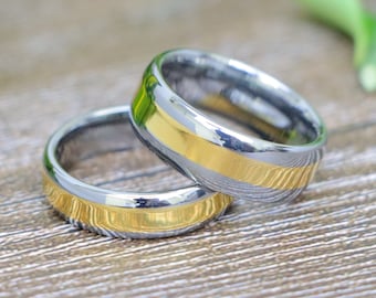 May include: Two silver wedding bands with a gold inlay. The bands are stacked on top of each other.