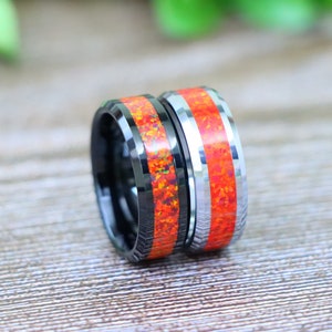 May include: Two black tungsten carbide rings with a red and orange opal inlay. The rings are beveled and have a polished finish.