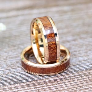 May include: Two gold tungsten carbide rings with a wood inlay. The rings are stacked on top of each other. The wood inlay is a dark brown color.