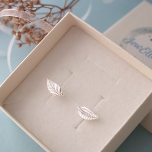 May include: A pair of silver leaf earrings in a white box. The earrings are small and delicate, with a simple design.