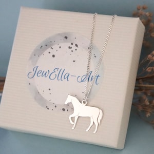 Op de afbeelding: Een zilveren paardenhangerketting in een witte doos met de tekst "JewElla-Art" erop.