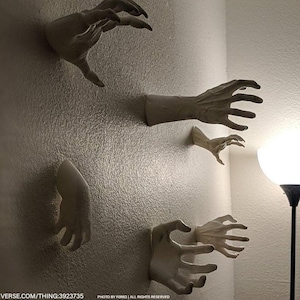 May include: Five white, sculpted hands protrude from a textured wall. The hands are in different positions, with fingers extended and curved, creating a spooky, artistic display. The hands are a light, neutral colour.