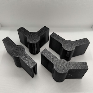 May include: Four black plastic corner brackets, each with a rounded corner and a flat surface. The brackets are designed to be used for joining two pieces of wood or other materials at a 90-degree angle.