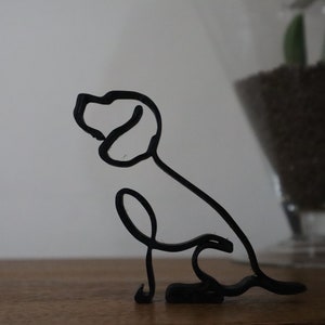 May include: A black wire sculpture of a dog sitting with its head turned to the side.