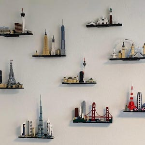 Puede incluir: Una colección de miniaturas de rascacielos de ciudades hechas con ladrillos LEGO, expuestas en estantes contra una pared blanca. Los rascacielos incluyen monumentos como la Torre Eiffel, el Empire State Building y la Tokyo Skytree.