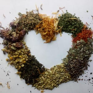 May include: A heart-shaped arrangement of various dried herbs and flowers, including chamomile, mint, and saffron, against a white background. The assortment showcases a range of colors and textures, suggesting a natural, botanical theme.