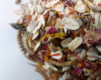 May include: A close-up of a mixture of dried flower petals, oats, and seeds. The mixture is a light brown color with hints of pink, yellow, and orange.