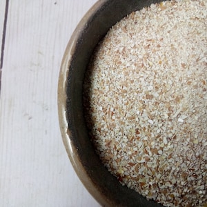 May include: A close-up of a brown bowl filled with a white, grainy substance. The substance appears to be a type of ground grain or flour.