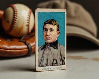 May include: A vintage baseball card featuring a portrait of a baseball player in a white uniform with a blue "D" on the chest. The card has a blue background and the text "WAGNER, PITTSBURG" at the bottom.