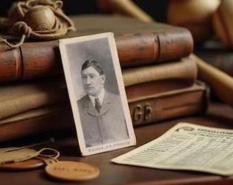 May include: Vintage baseball memorabilia featuring a Honus Wagner trading card, a baseball, and a score sheet. The card displays a black and white portrait of Wagner. The items are arranged on a wooden surface with old books in the background.