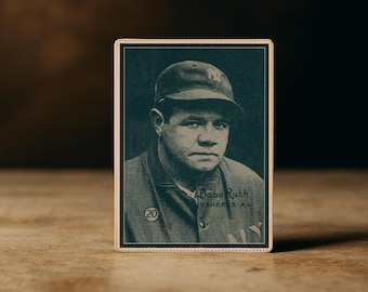 May include: Vintage baseball card featuring a sepia-toned portrait of Babe Ruth in a Yankees uniform. The card has a dark border and includes the text "Babe Ruth" and "Yankees A.L."