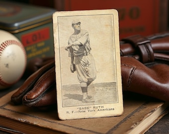 May include: Vintage baseball card featuring a black and white image of Babe Ruth in a baseball uniform. The card is aged with visible wear and tear. The text "BABE RUTH" and "R. F.—New York Americans" are printed at the bottom.