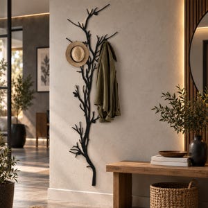May include: A black wall-mounted coat rack shaped like a bare tree branch with multiple hooks. A tan straw hat hangs on one of the upper branches, and an olive green jacket is draped over another branch, utilizing the structure for storage.