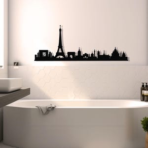 May include: Black metal silhouette of the Paris skyline, including the Eiffel Tower, Arc de Triomphe, and other famous landmarks. The silhouette is mounted on a white wall above a white bathtub in a bathroom.
