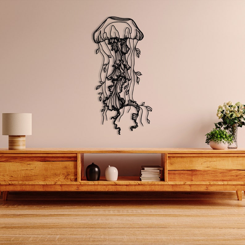 May include: Black metal wall art sculpture of a jellyfish with flowing tentacles and leaves. The sculpture is mounted on a light beige wall above a wooden entertainment center.