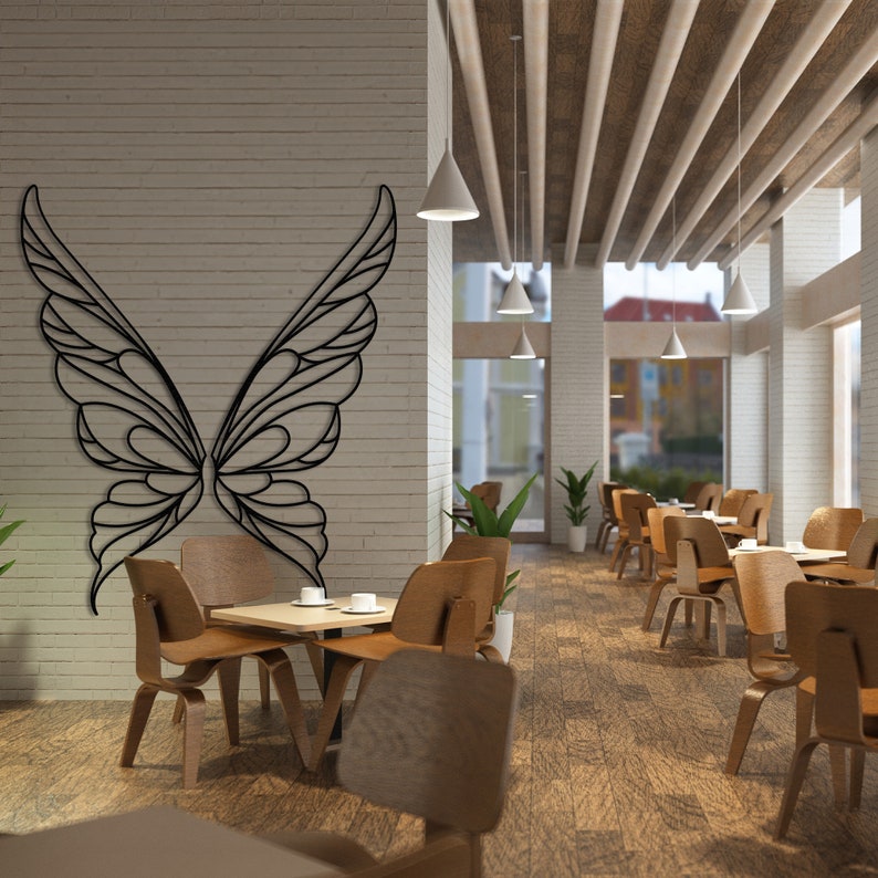 K&ouml;nnte beinhalten: Schwarze Metall-Wandkunst in Form von Schmetterlingsfl&uuml;geln schm&uuml;ckt eine Backsteinmauer in einem Caf&eacute;. Das Caf&eacute; verf&uuml;gt &uuml;ber Holztische und -st&uuml;hle, Pendelleuchten und eine Decke aus Holzbrettern. Die Schmetterlingsfl&uuml;gel sind symmetrisch und detailliert.