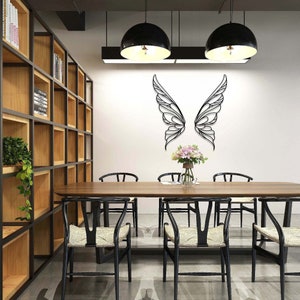 K&ouml;nnte beinhalten: Schwarze Metall-Wandkunst mit Schmetterlingsfl&uuml;geln. Die Fl&uuml;gel sind an einer wei&szlig;en Wand &uuml;ber einem Esstisch aus Holz mit sechs schwarzen St&uuml;hlen angebracht. Auf dem Tisch steht eine Vase mit Blumen. Der Raum hat ein modernes Design.