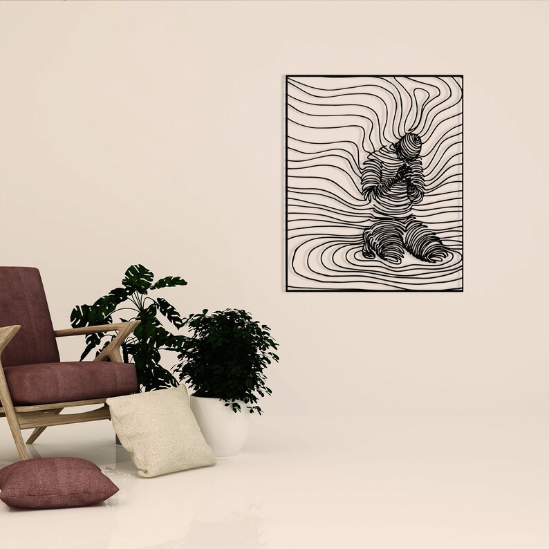 Op de afbeelding: Zwarte metalen wandkunst met een gestileerde lijntekening van een persoon die knielt met gevouwen handen in gebed. De kunst is geplaatst tegen een achtergrond van golvende lijnen.