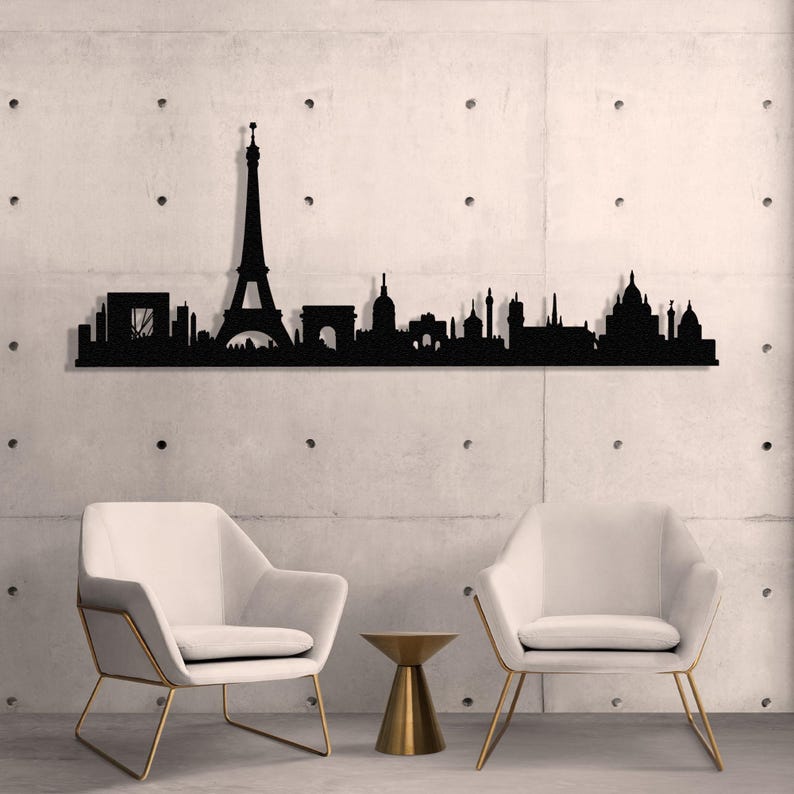 May include: Black metal silhouette of the Paris skyline, featuring the Eiffel Tower, Arc de Triomphe, and other iconic landmarks. The silhouette is mounted on a wall above two white chairs and a gold side table.
