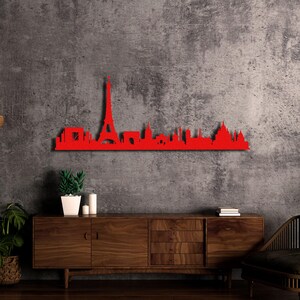 May include: Red metal Paris skyline wall art featuring the Eiffel Tower and other iconic landmarks. The art is mounted on a wall above a wooden dresser.