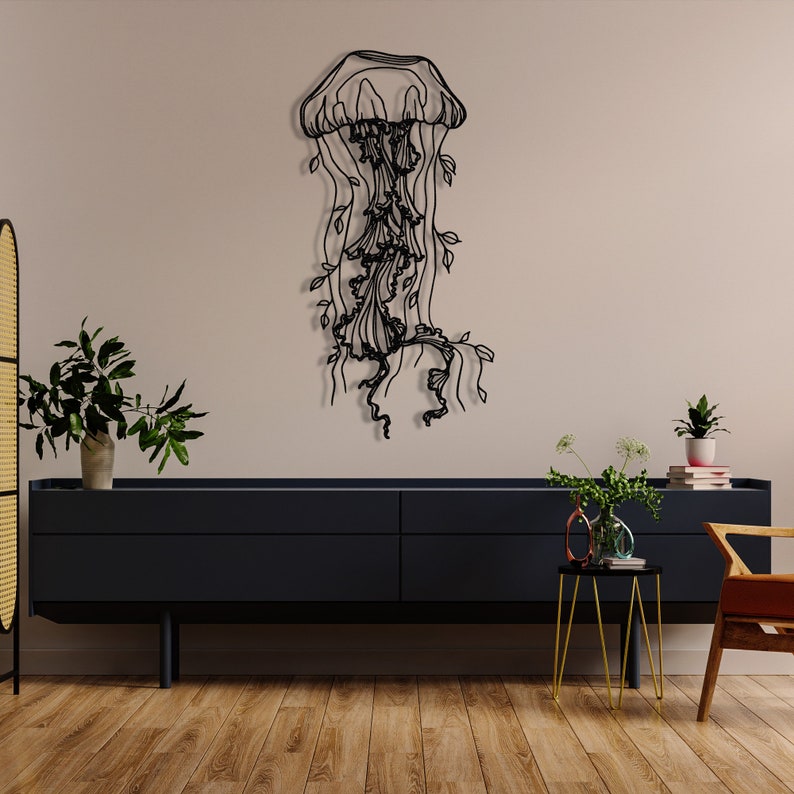 May include: Black metal wall art sculpture of a jellyfish with flowing tentacles and leaves. The sculpture is mounted on a light beige wall above a dark grey dresser.