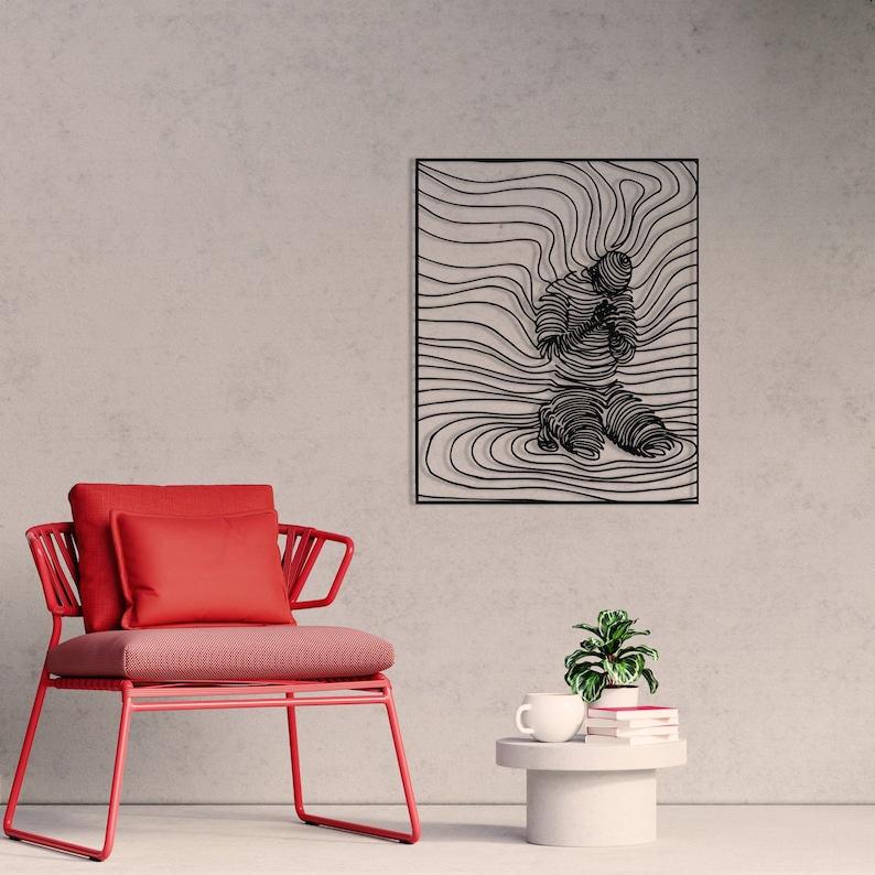 Op de afbeelding: Zwarte metalen wandkunst met een gestileerde figuur in een knielende houding, omringd door abstracte lijnen. De kunst is ingelijst en hangt aan een lichtgrijze muur.