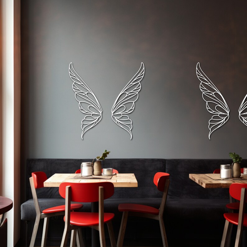 K&ouml;nnte beinhalten: Wei&szlig;e, lasergeschnittene Wandkunst in Form von Schmetterlingsfl&uuml;geln. Die Fl&uuml;gel werden paarweise mit filigranen Details und einem zarten, luftigen Design dargestellt. Sie sind an einer dunkelgrauen Wand angebracht und bilden einen auff&auml;lligen Kontrast.