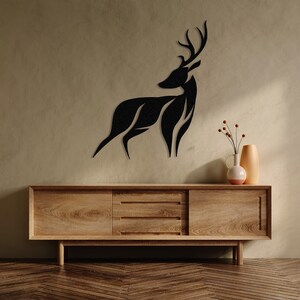 May include: A black silhouette of a deer with antlers mounted on a light brown wall above a wooden dresser with two drawers.