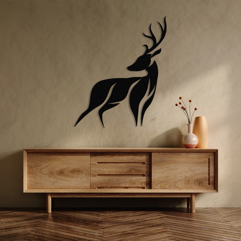 May include: A black silhouette of a deer with antlers mounted on a light brown wall above a wooden dresser with two drawers.