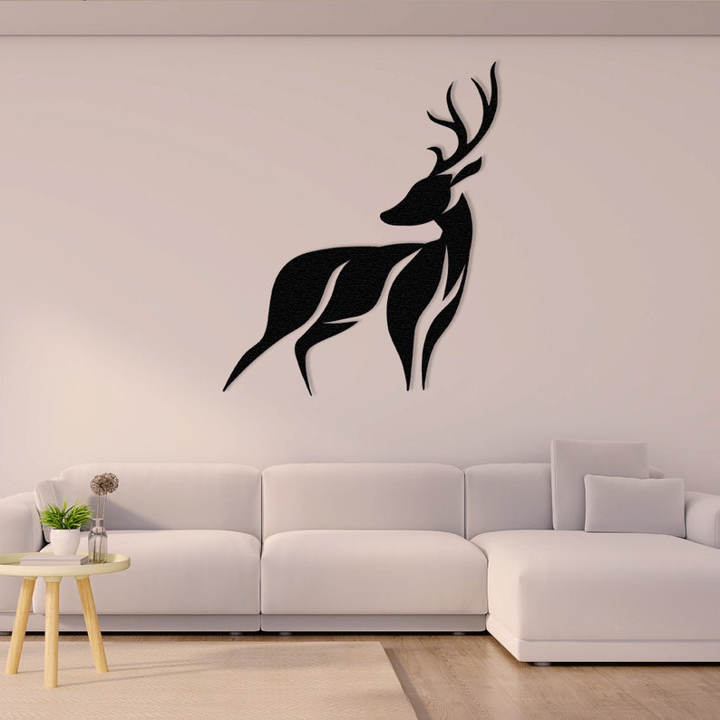 May include: Black silhouette of a deer with antlers, mounted on a white wall above a white couch. The deer is facing the right side of the image.