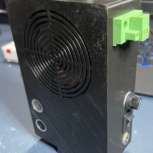May include: A black speaker with a round speaker grille, two small round holes, a green terminal block, a knob, a switch, and a jack.