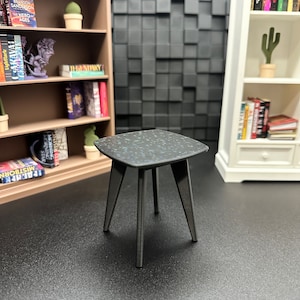 May include: A black side table with a speckled blue top and four legs. The table is in a room with bookshelves and a cactus.