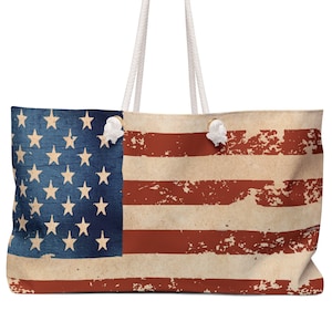 May include: A large tote bag with white rope handles and a distressed American flag design. The flag is red, white, and blue with a faded, vintage look.