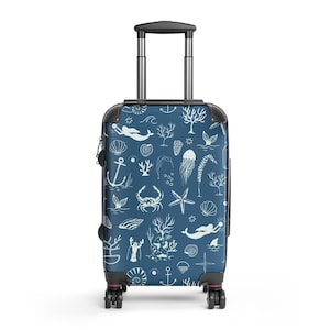 May include: A navy blue rolling suitcase with a white nautical pattern featuring mermaids, seashells, anchors, coral, and marine life. The suitcase has a retractable handle and black trim.