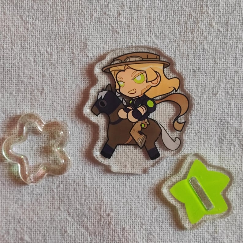 May include: Clear acrylic charm depicting a cartoon character on a brown horse. The character has blonde hair, a hat, and green eyes. Also included are a clear cloud-shaped charm and a green star-shaped charm with a silver bar.