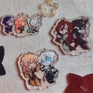 May include: Clear acrylic charms depicting anime-style characters. The charms feature characters with colourful hair, including purple, orange, white, red, and blonde. A clear star-shaped charm is also visible.