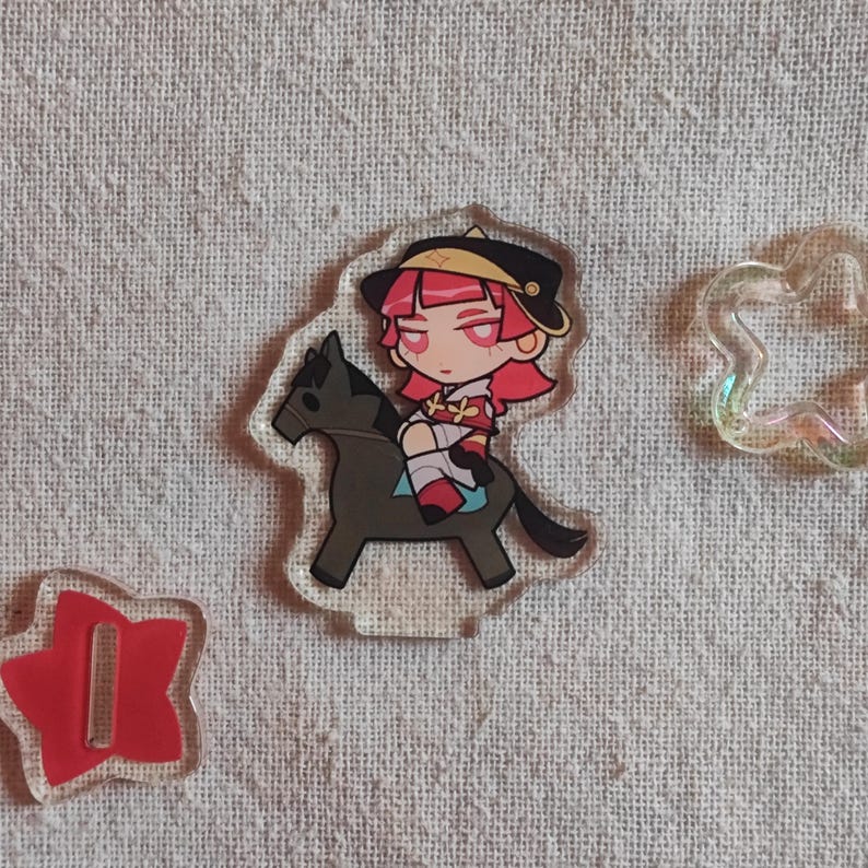 May include: A clear acrylic charm depicting a cartoon character with pink hair and a black hat riding a grey horse. A red star-shaped charm and a cloud-shaped charm are also visible.