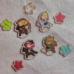 May include: A selection of clear acrylic charms depicting anime-style characters riding horses. The charms are accompanied by star-shaped acrylic pieces in shades of green, pink, and blue. The characters have detailed designs and bright colours.