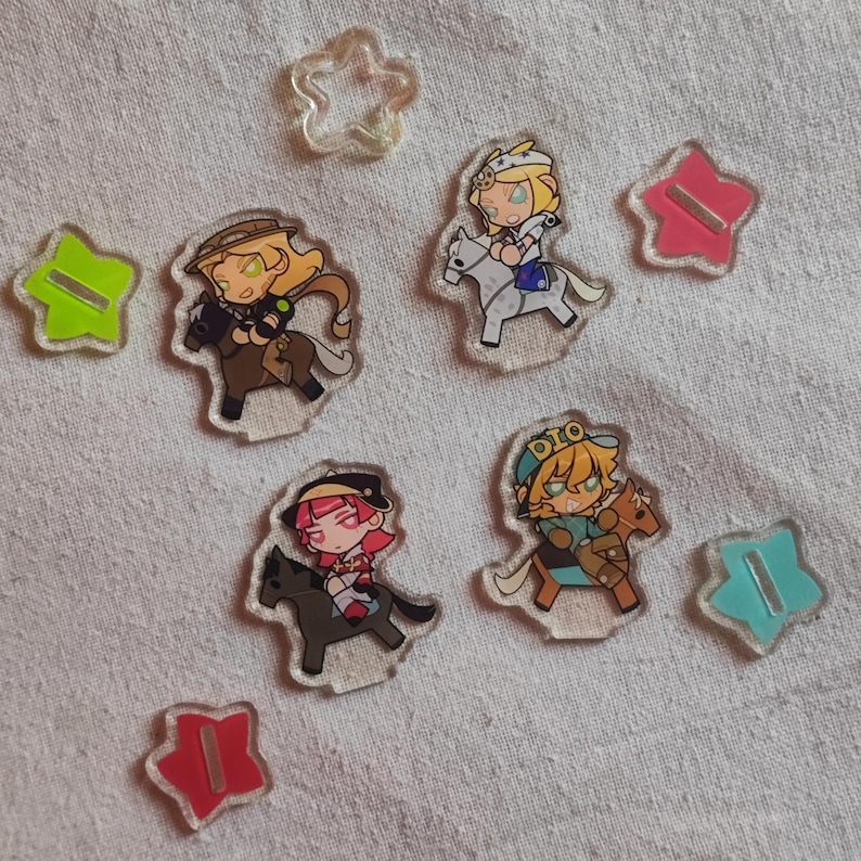 May include: A selection of clear acrylic charms depicting anime-style characters riding horses. The charms are accompanied by star-shaped acrylic pieces in shades of green, pink, and blue. The characters have detailed designs and bright colours.