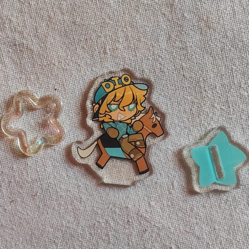 May include: Clear acrylic charms. One features a cartoon character on a horse, wearing a blue hat with "DIO" on it. There is also a clear star-shaped charm and a light blue star-shaped charm.