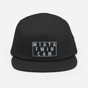 Puede incluir: Gorra negra de 5 paneles con una caja blanca y el texto "MIATA TWIN CAM" en gris.
